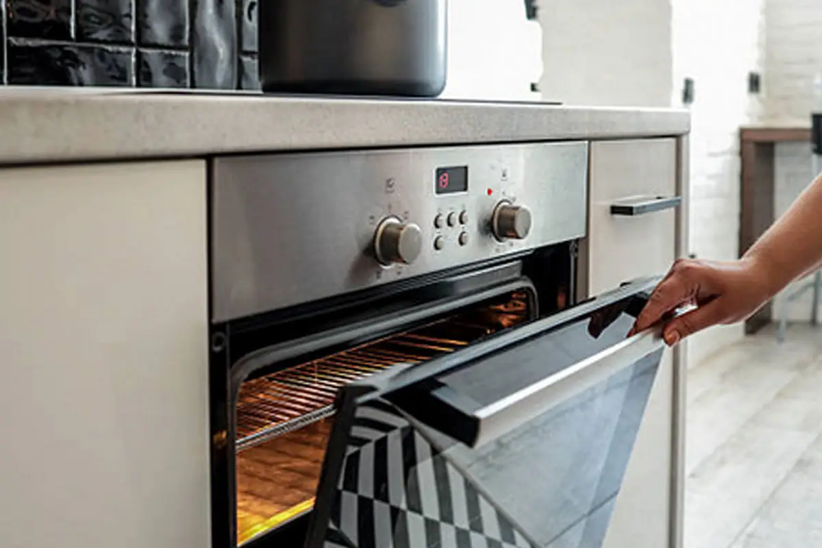 Hand opening the door of a stainless steel oven with the light on inside
